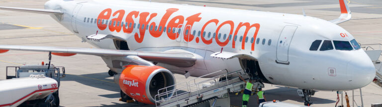 Doing No Harm Easyjet airplane parked at an airport terminal with a mobile staircase attached, and ground crew nearby.