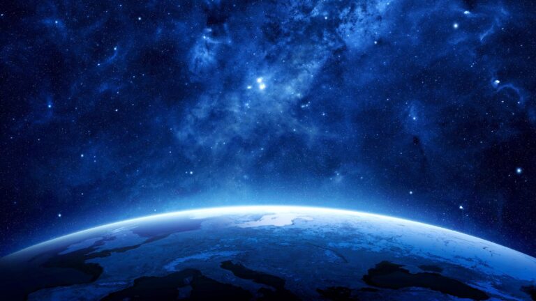 Image of Earth with a vast, star-filled space background. The curvature of the planet is visible, emphasizing the boundary between Earth's atmosphere and outer space. The sky is deep blue with scattered stars.