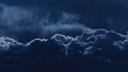 A night sky filled with dark clouds and numerous stars visible above.
