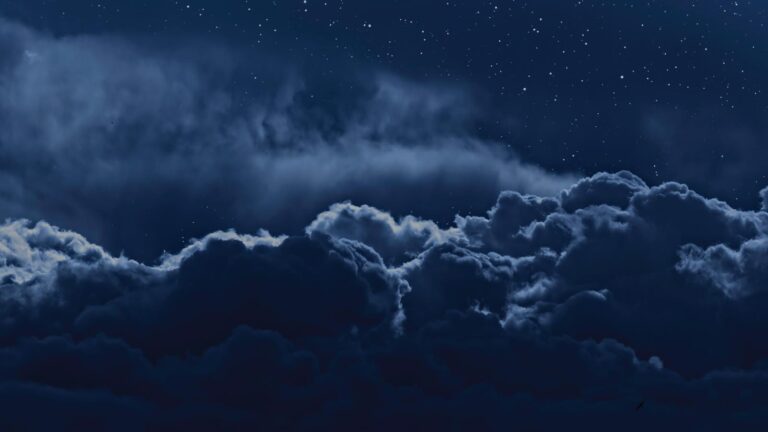 A night sky filled with dark clouds and numerous stars visible above.