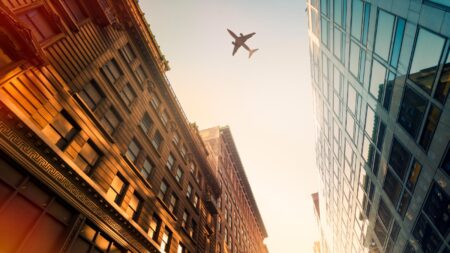 A plane flies overhead between two tall buildings at sunset.