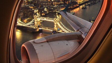 View of Tower Bridge in London from an airplane window, with the city's lights reflecting in the river below.