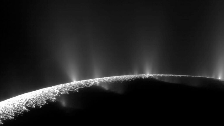 Black and white image of enceladus, a moon of saturn, showing icy geysers erupting from its surface.
