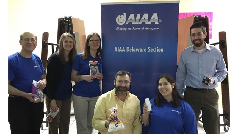 Group of six people posing with awards in front of an aiaa delaware section banner.
