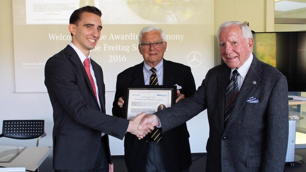 Two men shaking hands at an award ceremony, receiving a certificate from an older man, with a 