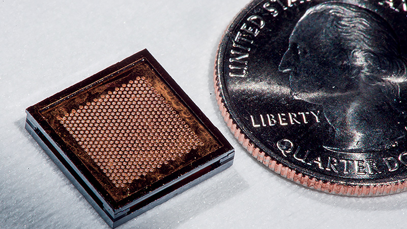 A close-up image of a small, square microchip next to a u.s. quarter to demonstrate scale.
