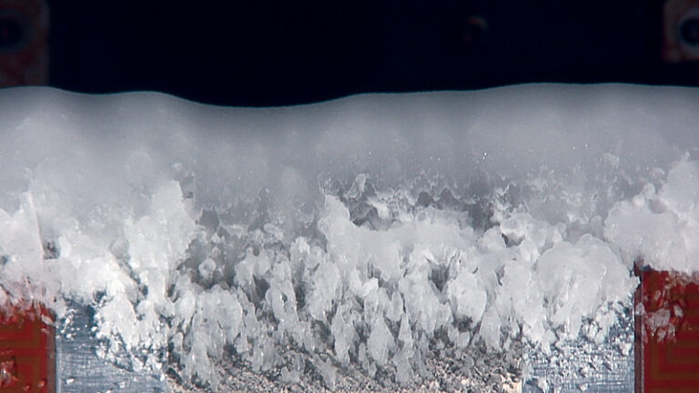 Close-up of a layer of snow and ice crystals accumulated on a red surface, with a blurred background.