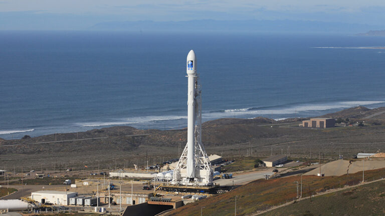 A rocket stands on the launchpad near the coast with the ocean in the background on a clear day.