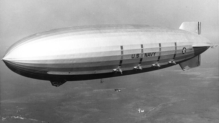 Black and white photo of a large u.s. navy airship flying in the sky.
