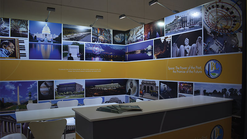Exhibition booth with a desk and panels displaying various images of landmarks and cultural scenes under the banner 