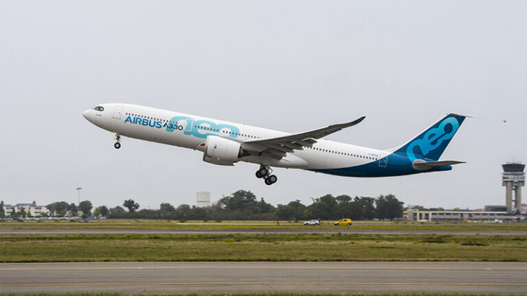 An airbus a330 aircraft, featuring a blue and white livery, takes off from an airport with a control tower in the background.