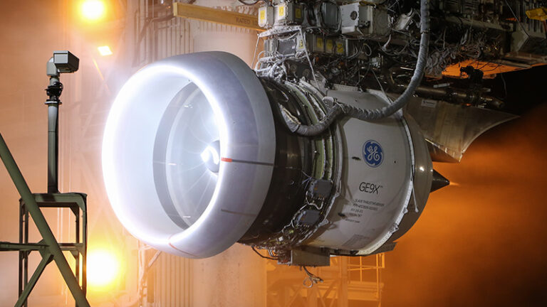 A ge9x jet engine undergoing a test run, illuminated by bright lights in an industrial testing facility.