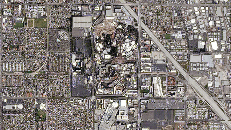 Aerial view of a densely built urban area with a large road intersection, featuring varied building sizes and open spaces.
