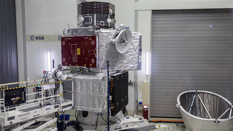 Satellite in a cleanroom environment with esa logo, equipped with instruments and metallic insulation, surrounded by testing equipment.