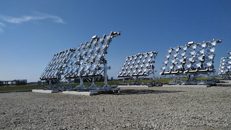 Array of heliostats in a solar power plant, with numerous circular mirrors mounted on adjustable panels under a clear blue sky.