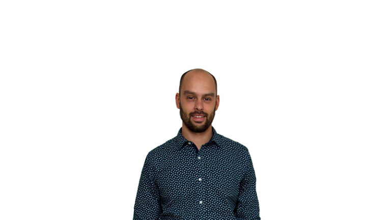 A bald man smiling at the camera, wearing a blue shirt with white dots, against a white background.