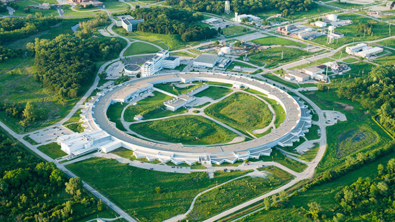 Aerial view of a circular scientific research facility surrounded by greenery and adjacent buildings.