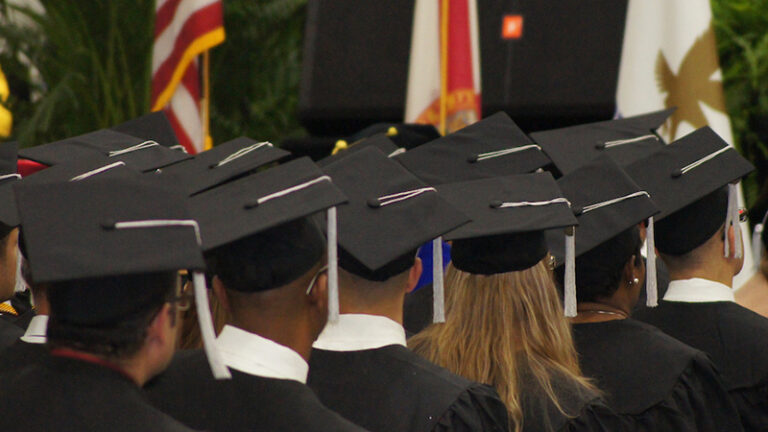 Back view of several graduates wearing traditional black caps at a graduation ceremony.
