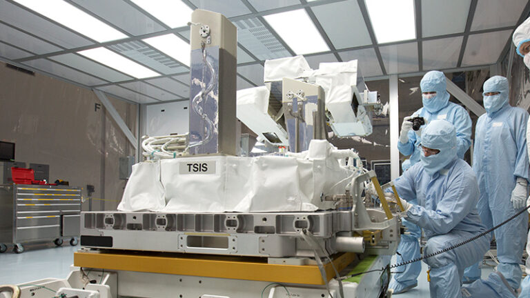 Engineers in cleanroom suits inspecting the tsis satellite instrument in a laboratory.
