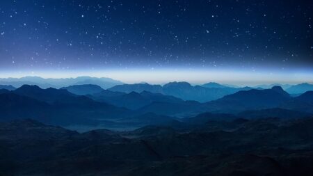 A serene night sky filled with stars above a range of dark, shadowy mountains.