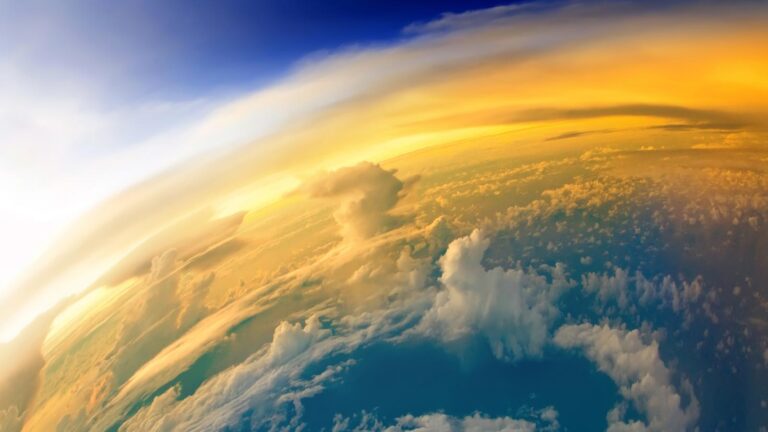 A view of Earth from space showing clouds, the curvature of the planet, and a dramatic yellow and blue sky gradient with the horizon extending across the image.