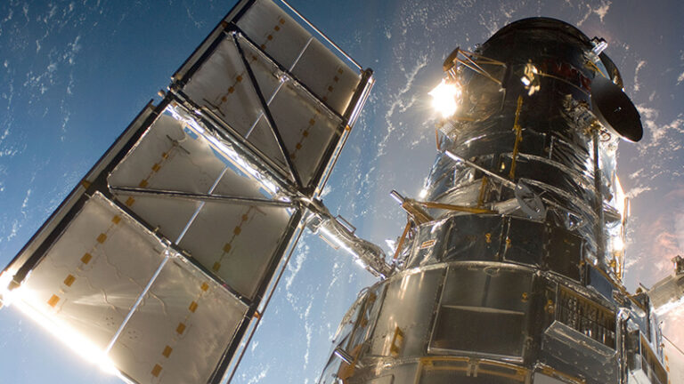 Close-up view of the Hubble Space Telescope against a backdrop of Earth and the blackness of space.
