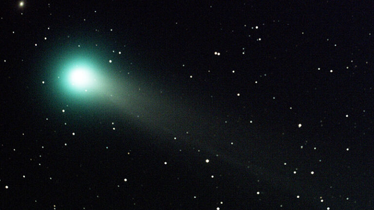 A bright green comet with a glowing tail moves through a star-filled night sky.