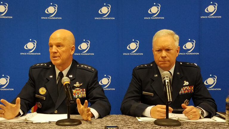 Two military officials in uniform sit at a table with microphones in front of a "Space Foundation" backdrop, engaged in a discussion.