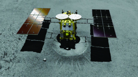 A spacecraft with solar panels on either side is positioned over a surface, likely a planetary body. There are noticeable shadows cast on the ground.