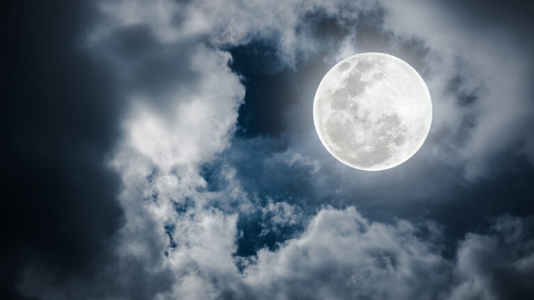 Full moon shining brightly in the night sky surrounded by clouds.
