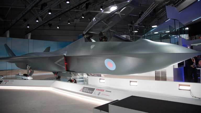 A grey military aircraft model named Tempest displayed indoors with its cockpit open, under overhead lights, and informational signage at the base.