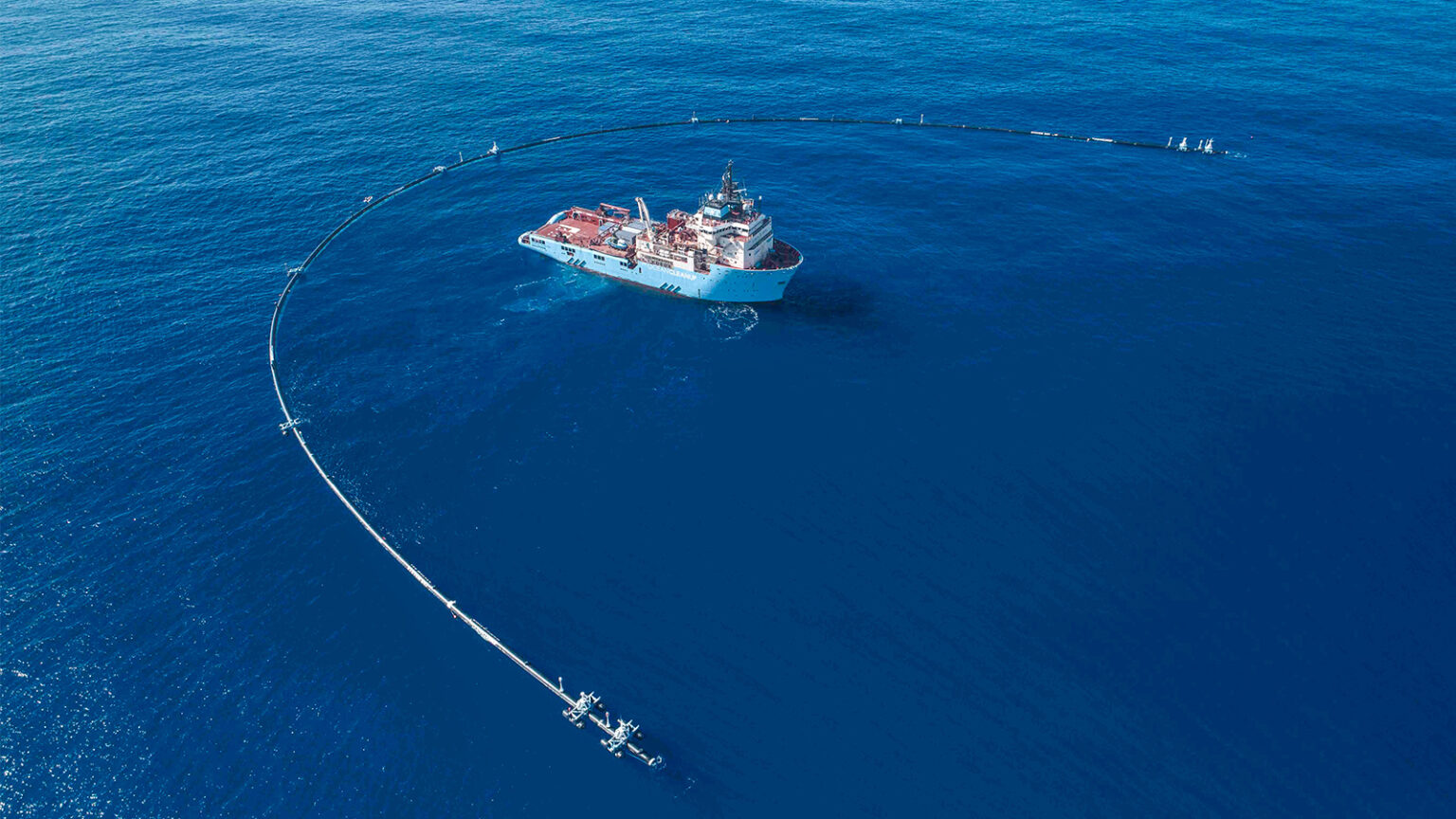 A ship is deploying a large floating barrier in the ocean as part of a marine debris collection system.