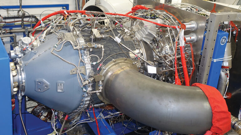 Close-up view of a complex industrial machine or engine with numerous wires, tubes, and components, indicating high-level mechanical engineering.