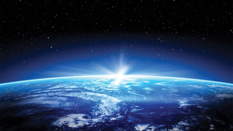 View of Earth from space with the sun rising over the horizon, casting a blue glow. Stars are visible in the background.