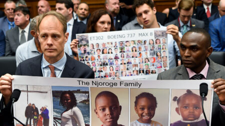 People at a hearing hold posters with photos of victims of the ET302 Boeing 737 Max 8 crash, including a specific family and a collage of other victims.