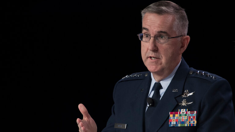 A man in a military uniform with multiple medals and ribbons speaks while gesturing with his left hand.