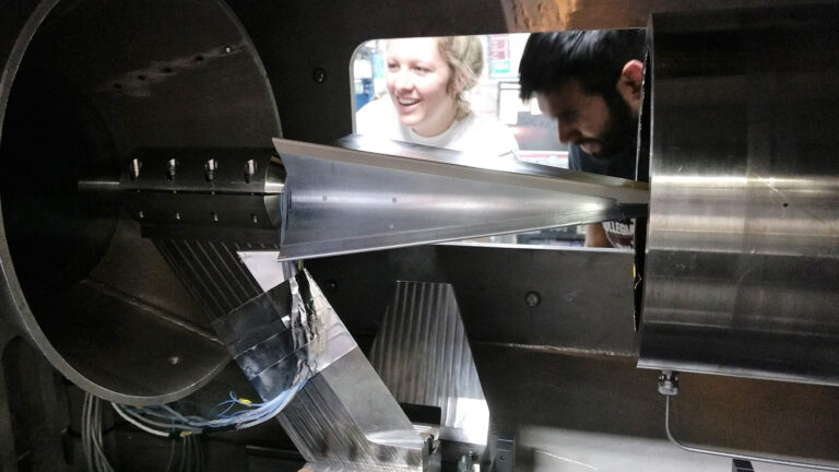 Two people are inspecting a large, metallic, industrial machine with intricate parts and mechanisms.