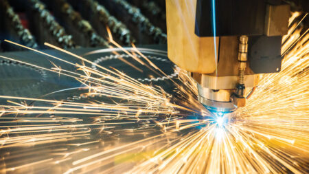 A close-up of a CNC laser cutting machine emitting bright sparks as it cuts through metal.