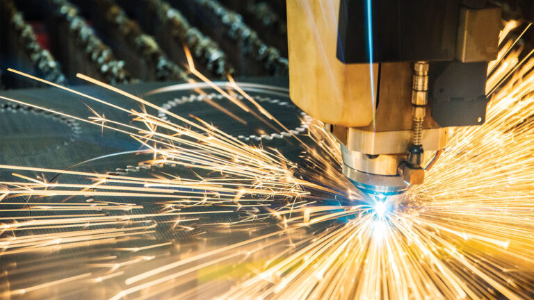 A close-up of a CNC laser cutting machine emitting bright sparks as it cuts through metal.