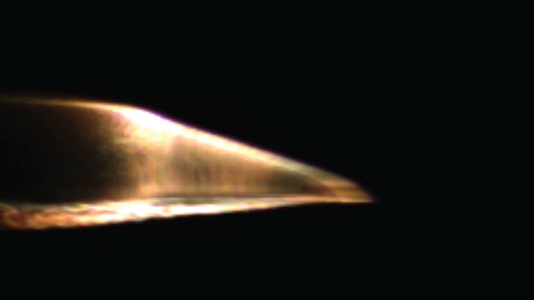 A close-up image of a metallic object with a sharp edge, illuminated against a dark background.