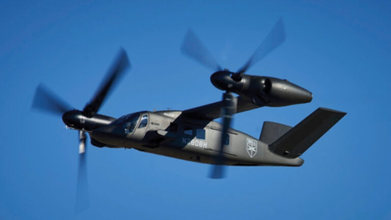 Aircraft with tilt-rotor propellers in mid-flight against a clear blue sky.