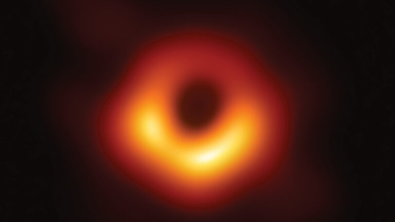 Blurred image of a black hole with a dark center and bright orange-yellow ring, captured by the Event Horizon Telescope.