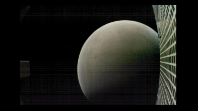 A spherical celestial body captured partially, with a grid structure visible on the right side of the image.