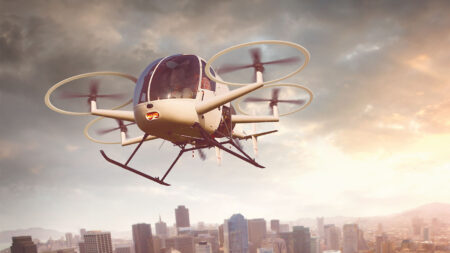 A flying drone taxi with multiple rotors hovers over a cityscape during sunset.