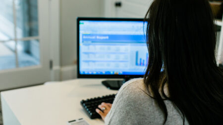 A person using a computer, viewing a detailed report on the screen in an office setting.