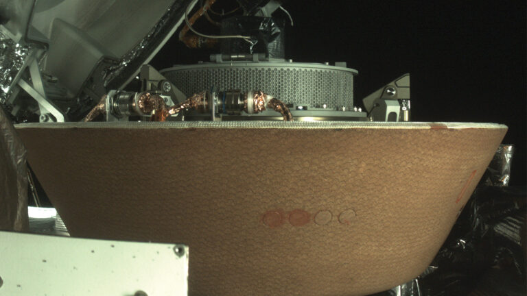 A close-up view of a spacecraft's sample return capsule, displaying its cone-shaped heat shield and various attached instruments, captured in space.