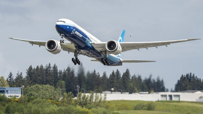A Boeing airplane takes off from a runway with trees and buildings in the background.