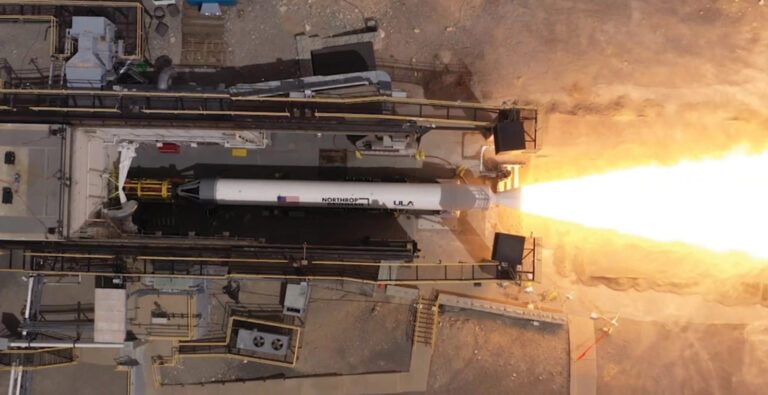 An overhead view of a rocket launching from a pad, showing flames and smoke as it propels upwards.