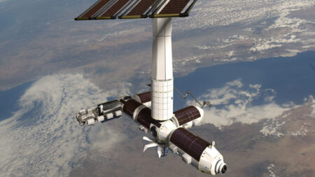 A space station orbits Earth, featuring large solar panels and several cylindrical modules connected by a central hub. White clouds and landmasses are visible on the Earth's surface below.