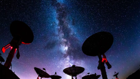 Silhouettes of satellite dishes under a starry night sky with the Milky Way visible in the background.
